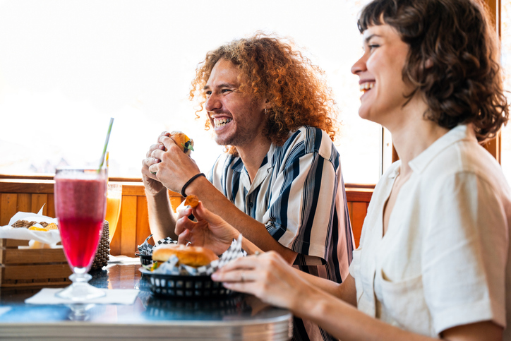 Multiethnic group of young happy friends bonding at vintage diner burger house restaurant - young friends are happily eating burgers and drinks together at a retro diner